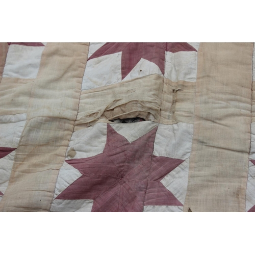 193 - An early 20th century quilt with thirty central star-shaped guls in shades of red and cream, 74 1/2