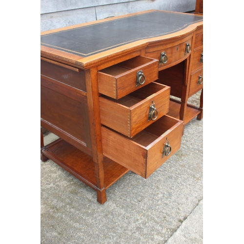 654 - An Arts & Crafts walnut break bowfront double pedestal desk with tooled lined top, fitted seven draw... 