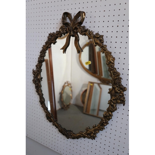 567 - An oval gilt metal framed wall mirror with floral decoration and ribbon finial, 17 3/4