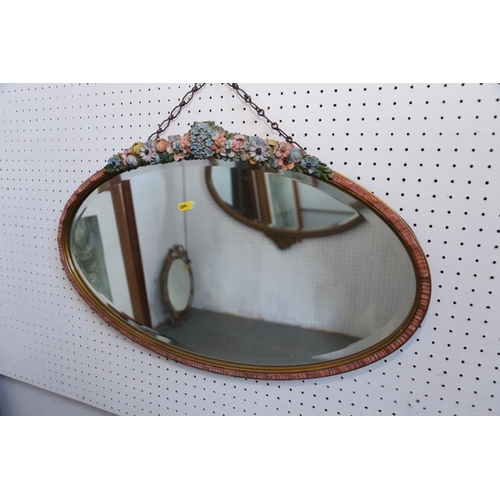 567 - An oval gilt metal framed wall mirror with floral decoration and ribbon finial, 17 3/4