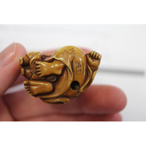 162 - A Japanese carved ivory netsuke Hotei with acolyte painting on his stomach, signed, 1 1/4