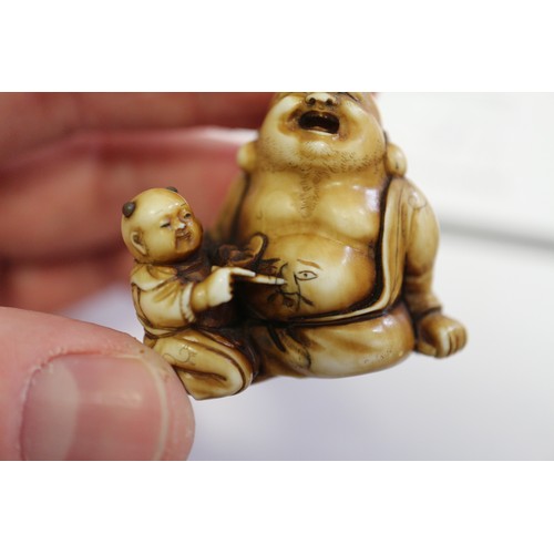 162 - A Japanese carved ivory netsuke Hotei with acolyte painting on his stomach, signed, 1 1/4