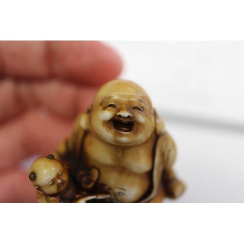 162 - A Japanese carved ivory netsuke Hotei with acolyte painting on his stomach, signed, 1 1/4