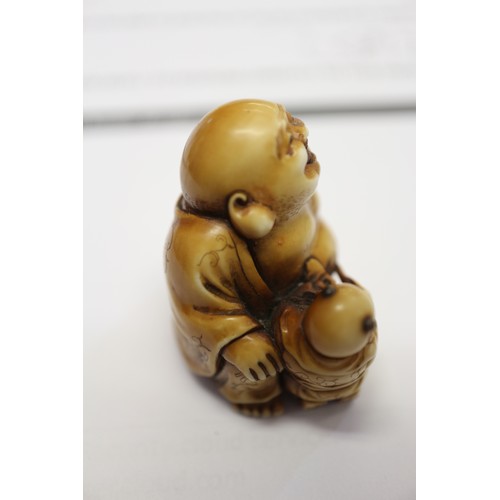 162 - A Japanese carved ivory netsuke Hotei with acolyte painting on his stomach, signed, 1 1/4