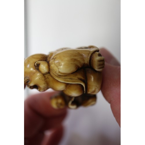 162 - A Japanese carved ivory netsuke Hotei with acolyte painting on his stomach, signed, 1 1/4