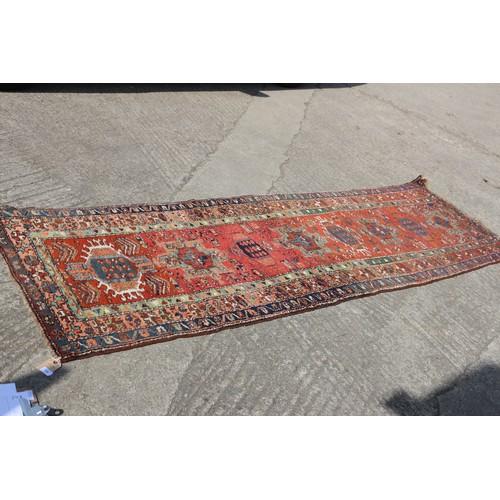 735 - A Kazak tribal runner with eight various guls/medallions on a cherry/rust ground and triple borders ... 