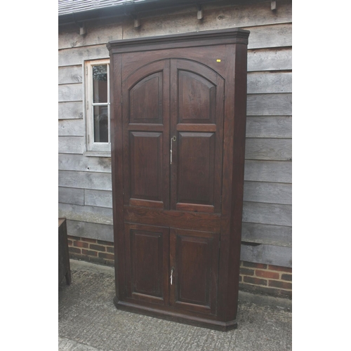 525 - An 18th century provincial oak corner cupboard, the shaped interior enclosed two arch top doors over... 