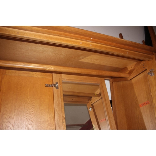 546 - A pair of Ercol light oak wardrobes enclosed panel doors with fitted interior mirror over one long d... 