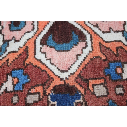 548 - A Hamadan carpet with central star design, on a salmon ground, in shades of blue, brown, pink, orang... 