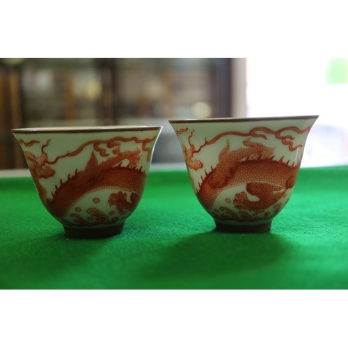 78 - A pair of Chinese iron red and white glazed tea bowls and saucers, decorated dragons and flaming pea... 