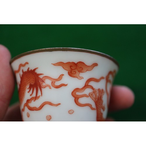 78 - A pair of Chinese iron red and white glazed tea bowls and saucers, decorated dragons and flaming pea... 