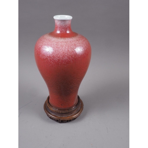 69 - A Chinese meiping red glazed vase, on hardwood stand, 10 3/4