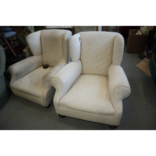 566 - A pair of deep seated wing armchairs, covered in a white figured brocade, on bun feet (one bun loose... 