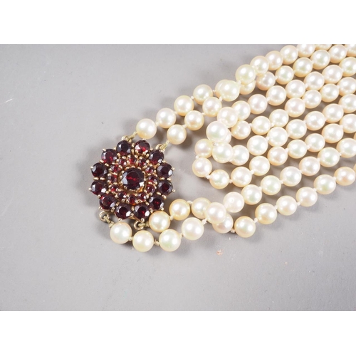 319 - A two-strand cultured pearl necklace with yellow metal and garnet cluster clasp, 46 1/2