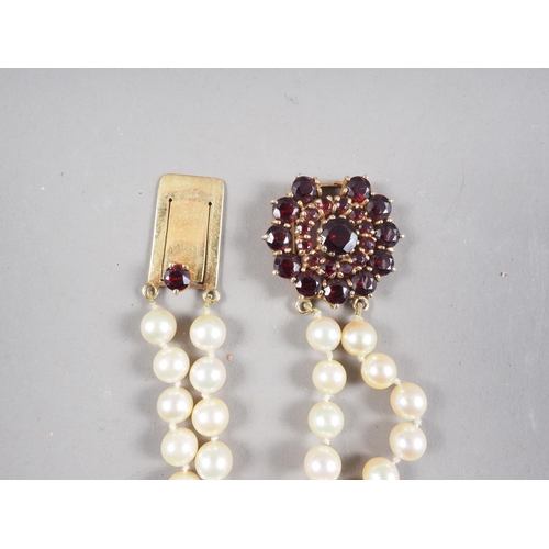 319 - A two-strand cultured pearl necklace with yellow metal and garnet cluster clasp, 46 1/2