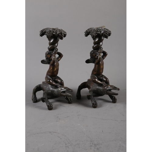 157 - A pair of 19th century bronze candlesticks, formed as putto seated on crocodiles, 8 3/4