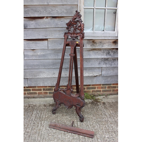 544 - An artist's carved hardwood saloon easel, on scroll supports