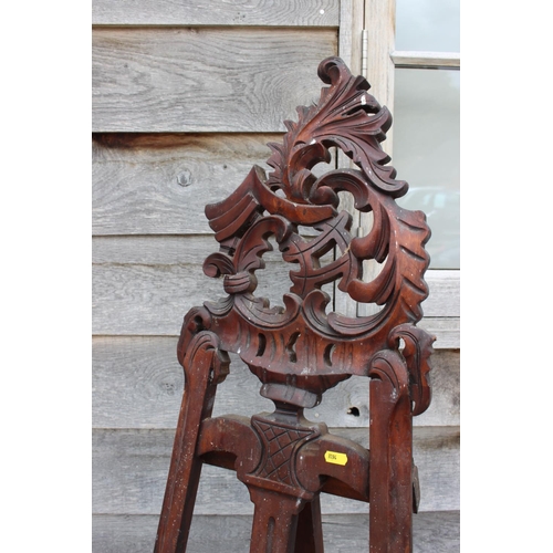 544 - An artist's carved hardwood saloon easel, on scroll supports