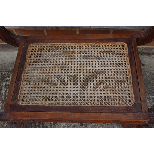 551 - An Anglo-Indian carved hardwood window seat of Regency design with cane seat, on reeded sabre suppor... 