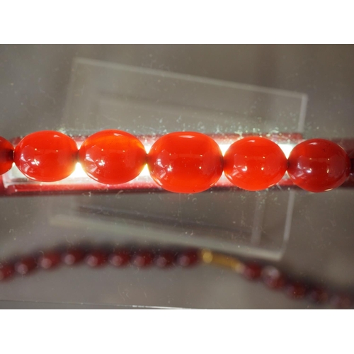 373 - An Art Deco cherry amber Bakelite necklace, the largest oval bead 12mm wide, 35.4g, and another simi... 