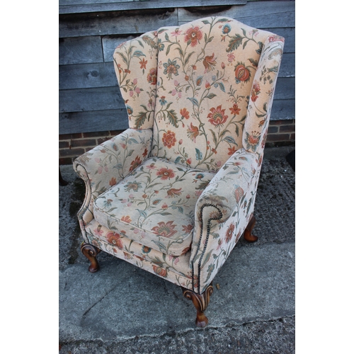 585 - A wing armchair of Georgian design with loose seat cushion, upholstered in a floral fabric, on cabri... 