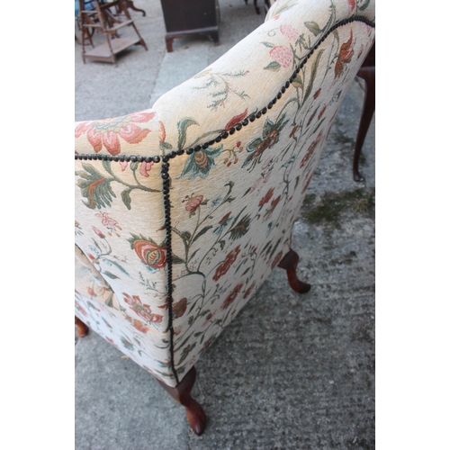 585 - A wing armchair of Georgian design with loose seat cushion, upholstered in a floral fabric, on cabri... 