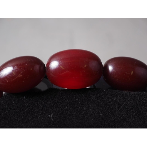 300 - A cherry amber Bakelite bead necklace, the largest oval bead, 29mm long, 64.4g gross