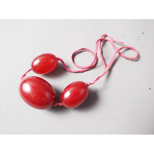 305 - Three cherry amber Bakelite beads, the largest oval bead, 40mm long, on silk thread, 45.6g gross