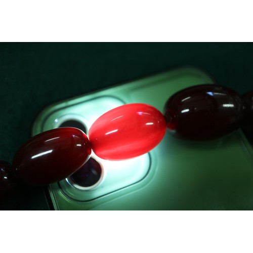 300 - A cherry amber Bakelite bead necklace, the largest oval bead, 29mm long, 64.4g gross