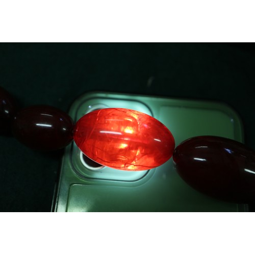 303 - A cherry amber Bakelite bead necklace, the largest oval bead, 37mm long, 61.8g gross and another sim... 