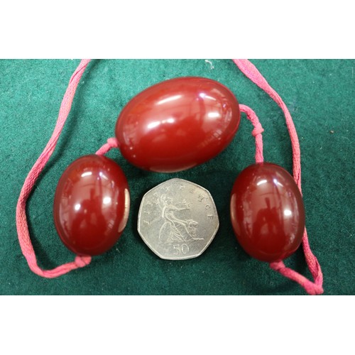 305 - Three cherry amber Bakelite beads, the largest oval bead, 40mm long, on silk thread, 45.6g gross