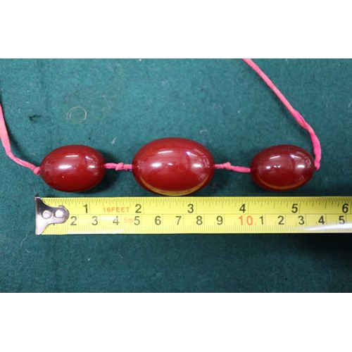 305 - Three cherry amber Bakelite beads, the largest oval bead, 40mm long, on silk thread, 45.6g gross