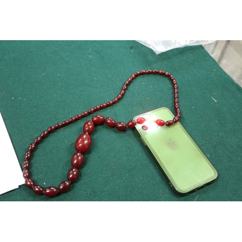 302 - A cherry amber Bakelite bead necklace, the largest oval bead, 34mm long, 71.6g gross, and another si... 