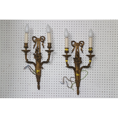 245 - A set of four gilt brass two-branch wall lights after Feloix with ribbon crests, 18