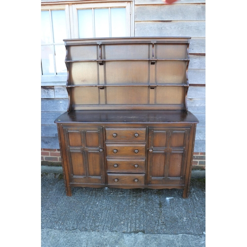 501 - An Ercol dark elm Old Colonial dresser with three-tier plate rack over four drawers and flanking cup... 