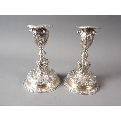 219 - A pair of Elkington silver plated candlesticks with relief and embossed classical decoration, on cir... 