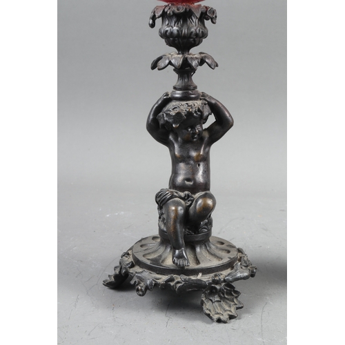 199 - A pair of early 19th century patinated candlesticks, formed as putti, with later added ruby glass oi... 