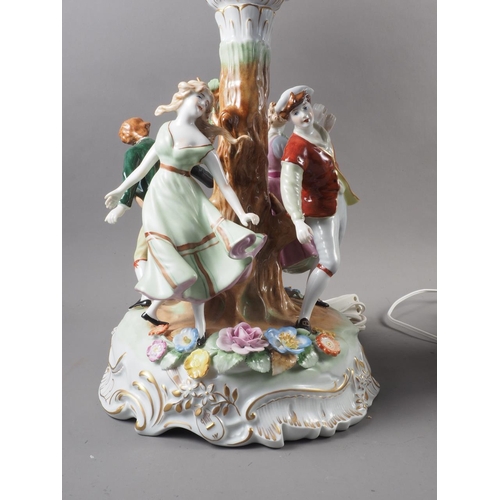 181 - A pair of Continental porcelain table lamps, the base decorated with figures dancing around a tree, ... 