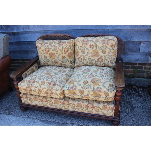 583 - A 1930s carved oak two-seat settee with cane back and loose seat and back cushions, on turned suppor... 