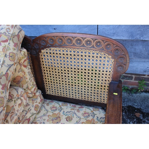 583 - A 1930s carved oak two-seat settee with cane back and loose seat and back cushions, on turned suppor... 