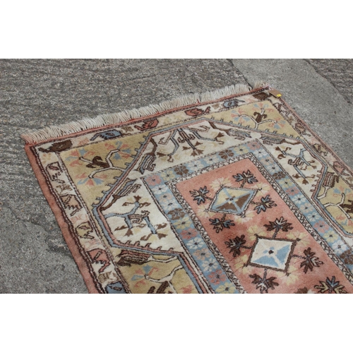 630 - A Kazak style wool pile rug with geometric design on a pink ground and multi-borders on a light grou... 