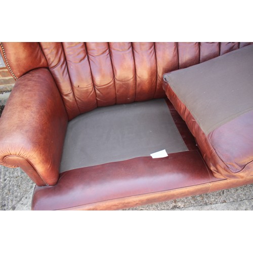 493 - A leather upholstered settee with two shaped cushions and twelve-panel shaped and stitched back, on ... 