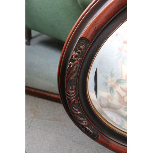 517 - An oval stained as mahogany and ebonised carved moulded frame wall mirror with bevelled plate, 27