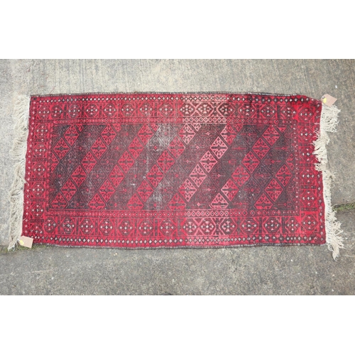 635 - A Baluchi rug with twelve hooked red guls and multi-borders in shades of red, black and white, 60