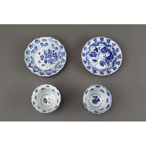 85 - Blue and White: Two Cups and Two Saucers, Kangxi the barbed moulded cups with panelled bird and flow... 