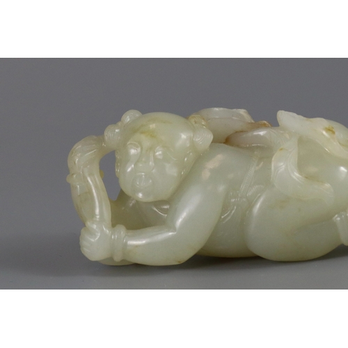 193 - A Pale Celadon Jade Boy, 18th century,  finely carved with the smiling reclining boy holding a leafy... 