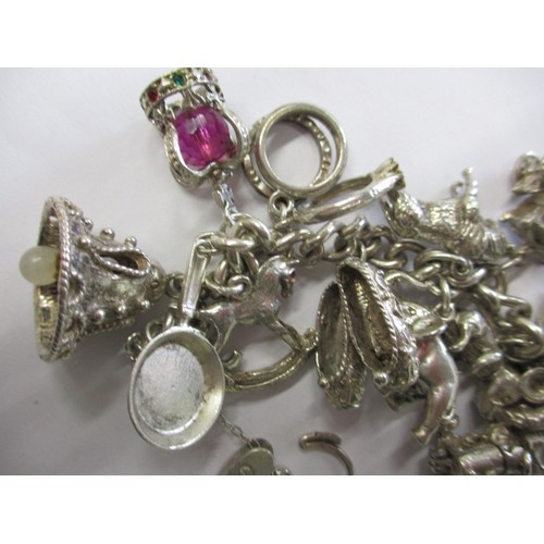 114 - A silver and white metal charm bracelet, approx. weight 90.5g having multiple charms in pre-owned co... 