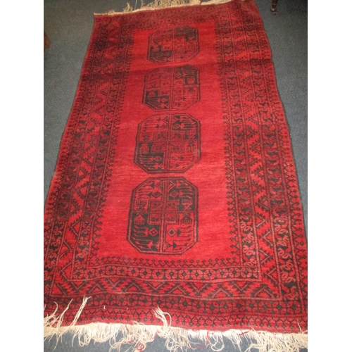 329 - A vintage hand woven Afghan wool rug, approx. size 216x125cm, having a rich red ground with black ge... 