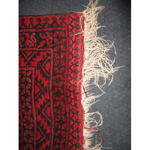 329 - A vintage hand woven Afghan wool rug, approx. size 216x125cm, having a rich red ground with black ge... 