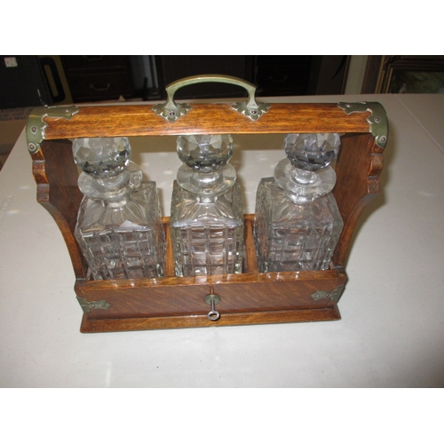 301 - An early 20th century oak 3 bottle tantalus, having key and working lock, in good used condition wit... 